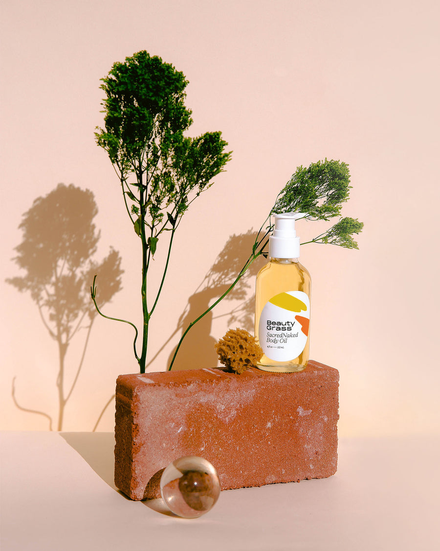 Body retinol alternative, SacredNaked body oil. On brick with plants.